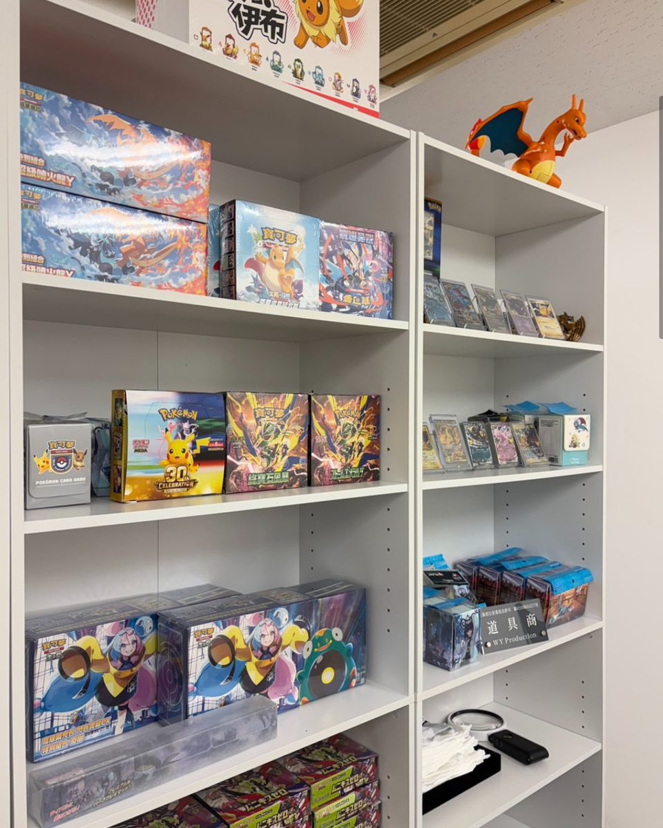 白い棚に並んだポケモンカードのBOXと鑑定済みカード。棚の上にリザードンのフィギュア